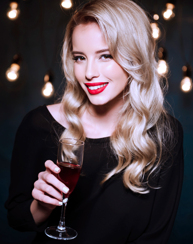 Beautiful blonde girl in evening dress smiling, holding wine gla